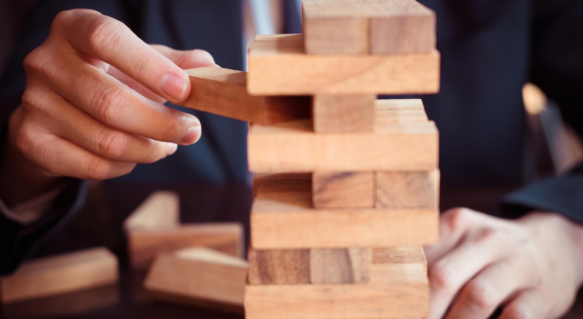 Man in a business suit removing Jenga blocks from a stack tower